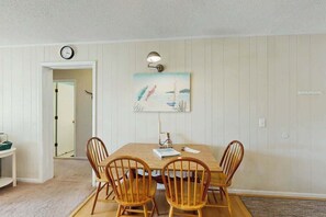 Un coin repas avec une table en bois et quatre chaises, une horloge murale et un tableau accroché au-dessus de la table.