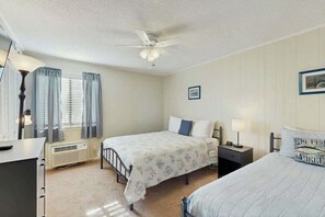 Une chambre avec deux lits, un ventilateur de plafond, un radiateur et une fenêtre avec des rideaux.