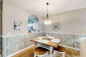 Ein Essbereich mit einem Holztisch und Stühlen, einer hängenden Leuchte und einer Wanddekoration mit Kompass.