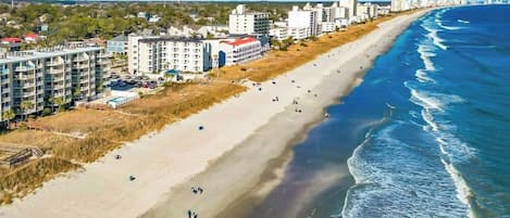 A coastal hotel with multiple floors, a sandy beach, and ocean views.