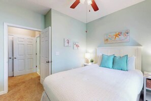 Een slaapkamer met een bed, een nachtkastje, een plafondventilator en een deur naar een andere kamer.