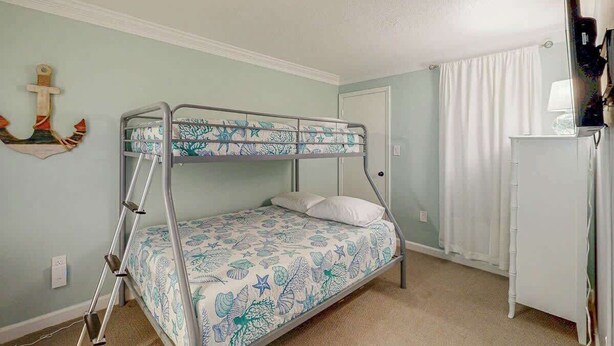Una cama individual superpuesta con una colcha estampada, un escritorio con una lámpara y una cortina en la ventana.