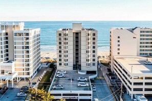 A multi-story hotel with a parking lot in front, situated near a beach with the ocean in the background. - Sea Marsh II Unit 1002 (North Myrtle Beach)