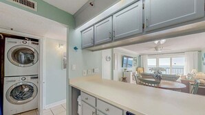 Una cocina con dos lavadoras apiladas, un comedor con una mesa redonda y vistas al salón.
