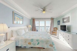 A bedroom with a bed, a ceiling fan, a television, and a view of the outdoors. - Sea Marsh II Unit 1002 (North Myrtle Beach)
