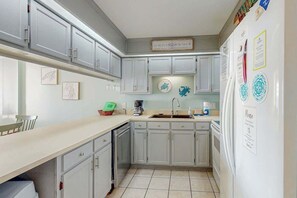 A kitchen with white cabinets, a sink, a refrigerator, and a coffee maker. - Sea Marsh II Unit 1002 (North Myrtle Beach)