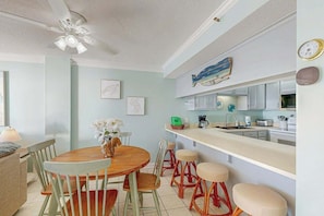 A dining area with a round wooden table, chairs, and a ceiling fan. - Sea Marsh II Unit 1002 (North Myrtle Beach)