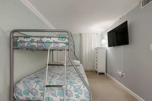 A bunk bed with a patterned bedspread, a television mounted on the wall, and a white dresser with drawers. - Sea Marsh II Unit 1002 (North Myrtle Beach)