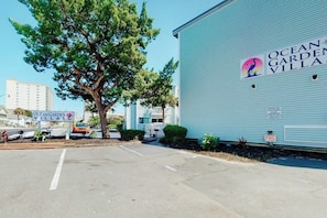 A building with a sign for Ocean Garden Villas, a parking lot, and a tree. - Ocean Garden Villas G-2 (North Myrtle Beach)