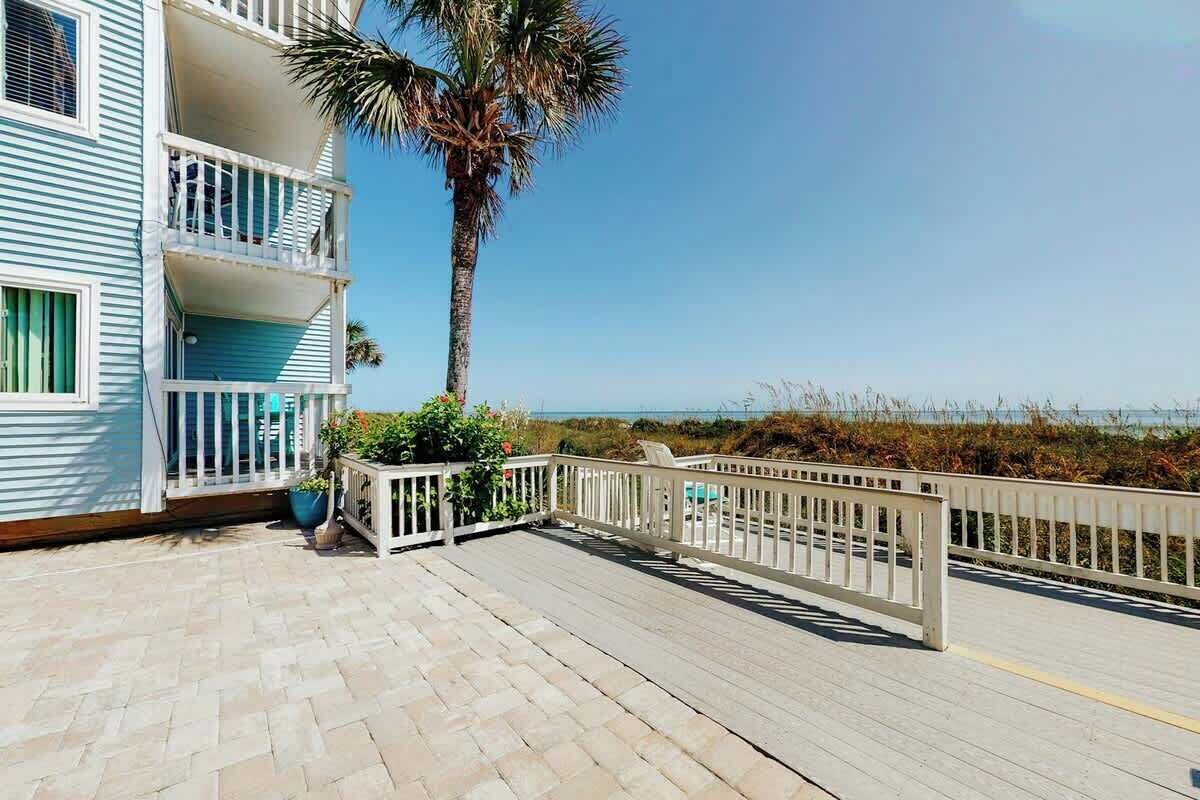 A beachfront property with a wooden deck, a palm tree, and a view of the ocean.