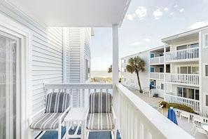 Ein Balkon mit zwei gestreiften Stühlen und einem kleinen Tisch, der Blick auf einen Strand und angrenzende Gebäude freigibt.