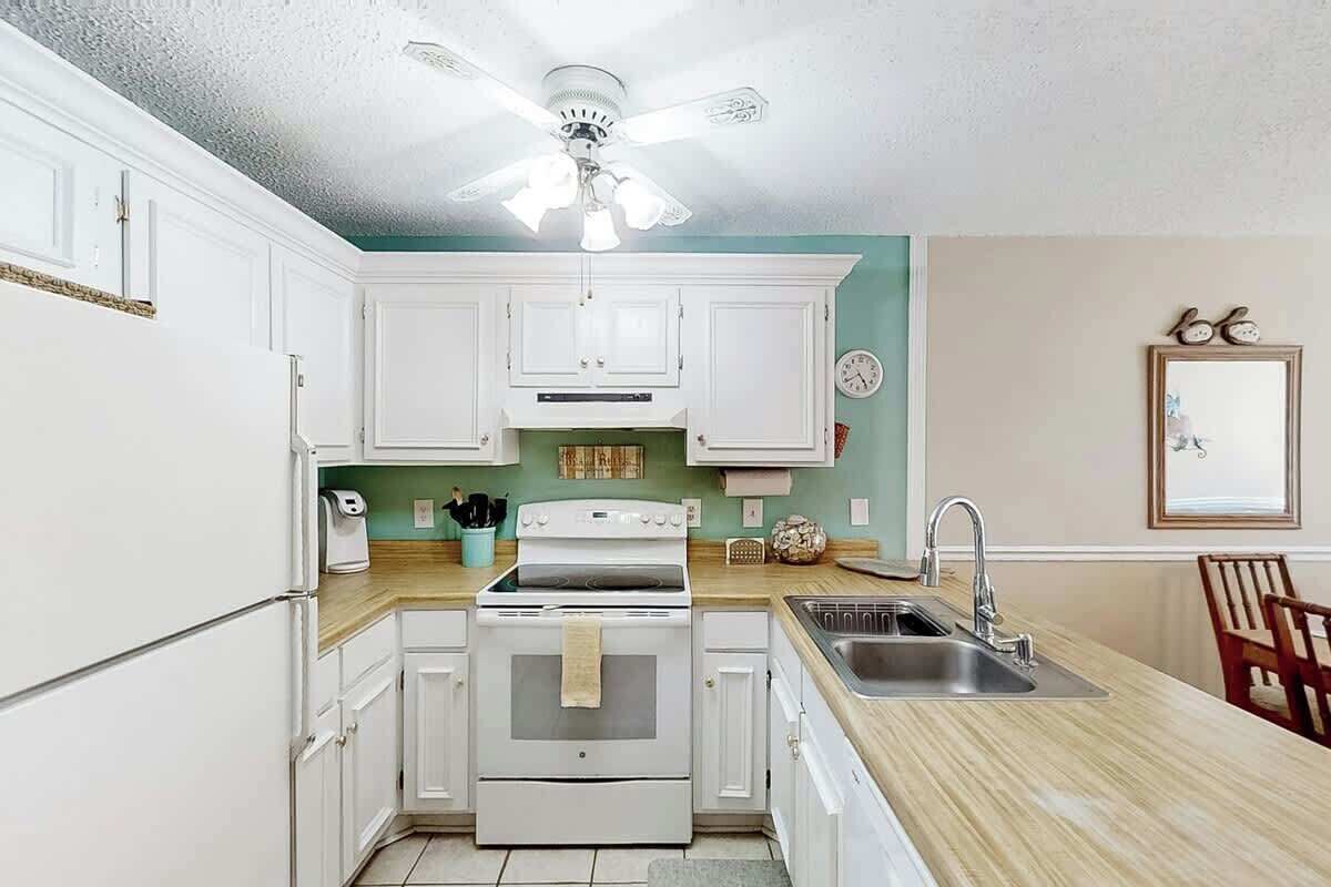 A kitchen with white cabinets, a stove, a sink, and a ceiling fan.