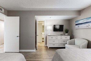 A hotel room with a bed, a TV mounted on the wall, a dresser, and a door leading to another room. - Sand Dunes Resort 2647 (Myrtle Beach)