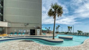 A swimming pool area with lounge chairs, a palm tree, and a building with a balcony. - Sand Dunes Resort 2647 (Myrtle Beach)