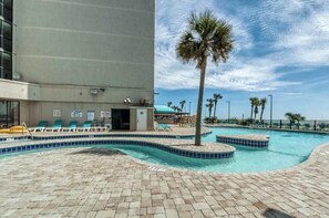 Área de piscina com espreguiçadeiras, uma palmeira e um edifício com varanda.
