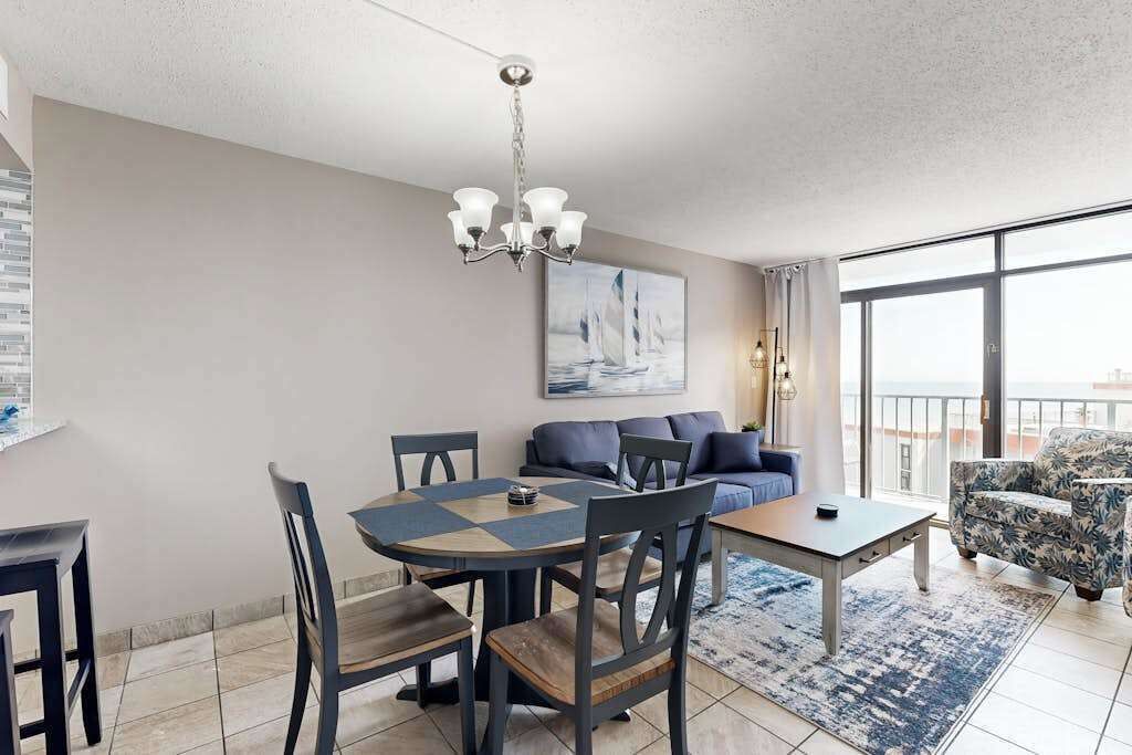 A modern living room with a dining area, a sofa set, and a large window providing a view.