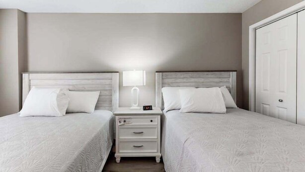 A hotel room with two beds, a nightstand with a lamp, and a door. - Sand Dunes Resort 2647 (Myrtle Beach)