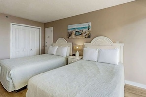 A bedroom with two beds, a nightstand, a painting, and a door. - Sand Dunes Resort 2648 (Myrtle Beach)