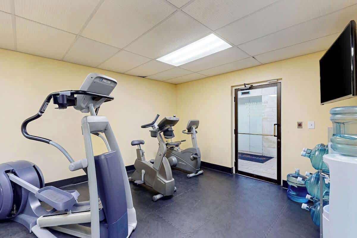 Une salle de sport équipée de machines de cardio, d’un distributeur d’eau et d’un téléviseur fixé au mur.