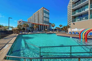 A swimming pool with lounge chairs and a building with multiple floors in the background. - Sand Dunes Resort 2648 (Myrtle Beach)