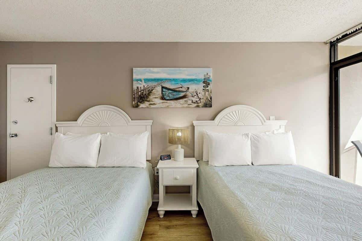 Een hotelkamer met twee bedden, een nachtkastje, een lamp en een schilderij van een strandgezicht.