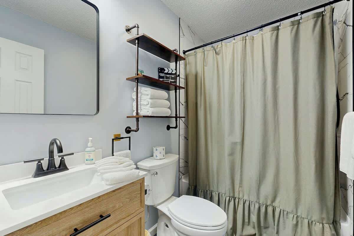 Ein Badezimmer mit weißem Waschbecken, Toilette, Spiegel und Duschvorhang.
