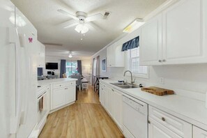 A modern kitchen with white cabinetry, a wooden floor, and a ceiling fan. - Hawleywood Too Retreat (Surfside Beach)