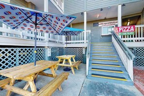 A wooden picnic table and benches under a Pepsi-branded umbrella, a pizza restaurant sign, and a staircase with yellow safety stripes. - Coffee with a View Retreat (Myrtle Beach)