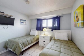 A bedroom with two single beds, a bedside table with a lamp, a flat-screen TV mounted on the wall, and a window with curtains. - Coffee with a View Retreat (Myrtle Beach)