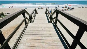 Une promenade en bois menant à une plage où se trouvent des gens et des parasols.