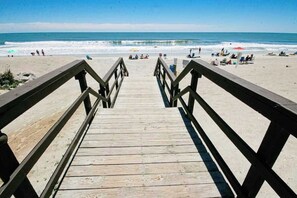 A wooden boardwalk leading to a beach with people and umbrellas. - Coffee with a View Retreat (Myrtle Beach)