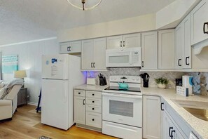 Une cuisine de taille réduite avec des meubles blancs, un four à micro-ondes, une cuisinière et un réfrigérateur.