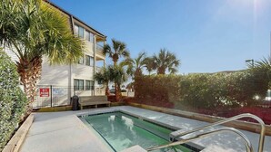 A swimming pool area with a bench, palm trees, and a building with a balcony. - Ocean Forest Villas A-216 (Myrtle Beach)