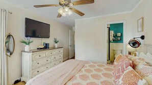 A bedroom with a bed, a ceiling fan, a dresser, a television, and a door leading to another room. - Ocean Forest Villas A-216 (Myrtle Beach)