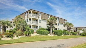 A multi-story residential building with balconies, surrounded by well-maintained lawns and palm trees. - Ocean Forest Villas A-216 (Myrtle Beach)