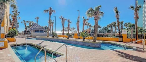 A swimming pool area with palm trees, a clear sky, and a building in the background.