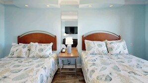 Hotellihuone, jossa on kaksi sänkyä, pieni pöytä, lamppu ja peili.