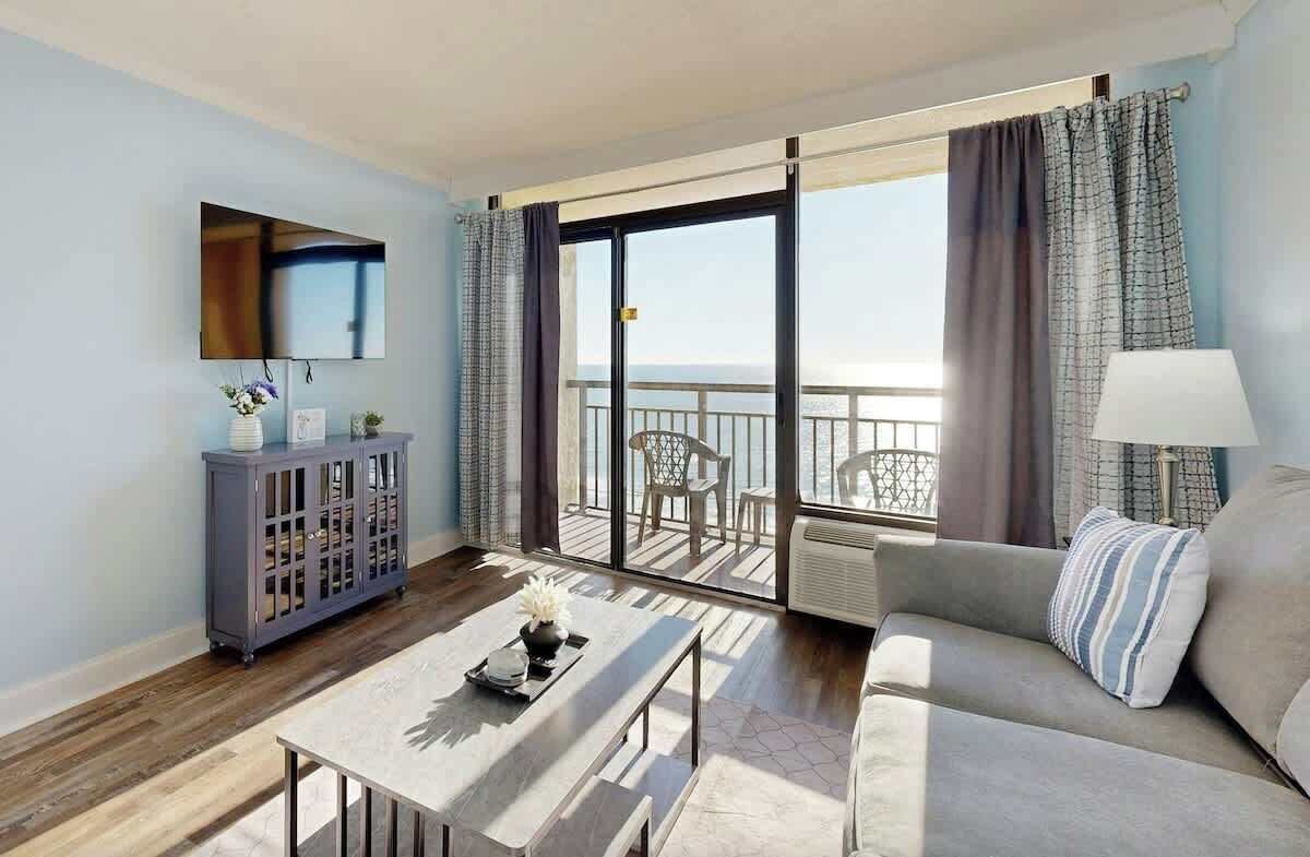 A modern living room with a sofa, a coffee table, a cabinet, and a balcony with a view of the sea.