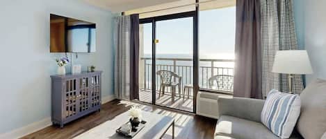 A modern living room with a sofa, a coffee table, a cabinet, and a balcony with a view of the sea.