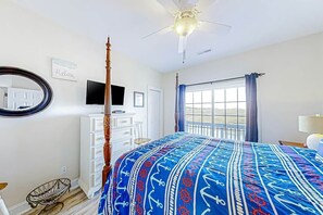 Ein Schlafzimmer mit Himmelbett, Deckenventilator, großem Fenster mit Vorhängen, Fernseher und weißem Schminktisch.