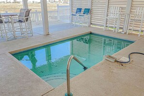 Ein Swimmingpool mit Metall-Geländer, umgeben von einer überdachten Terrasse mit weißen Stühlen und einem Tisch.