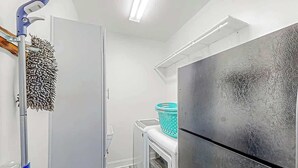 A compact kitchen with a refrigerator, a washing machine, and a mop. - Pointe Marsh Unit 2414 (North Myrtle Beach)