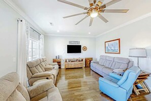 Ein Wohnzimmer mit Deckenventilator, Flachbildfernseher, Sofa, Liege- und Couchtisch.