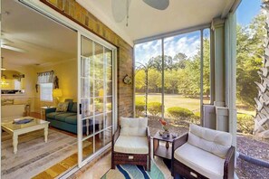 A sunlit room with a sliding glass door, a green sofa, a white armchair, and a small table with a vase. - 19th Hole Retreat Home (North Myrtle Beach)