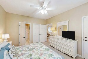 Camera da letto con letto, comò, televisore e ventilatore a soffitto.
