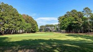 Un camp de golf sota un cel blau, envoltat de vegetació densa.