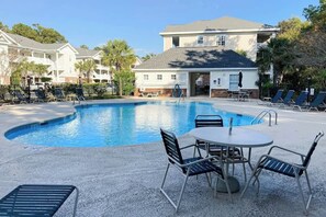A swimming pool with lounge chairs and a table, surrounded by a building with a balcony. - 19th Hole Retreat Home (North Myrtle Beach)