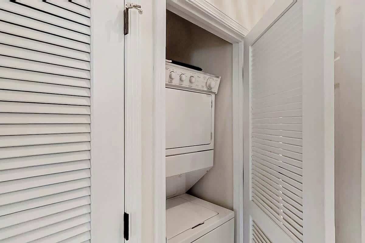 Un lavadero blanco con lavadora y secadora empotradas, una puerta con manija y un respiradero en la pared.