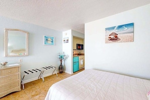 Un dormitorio con cama, cómoda, silla, mesita, espejo y un cuadro de una playa.