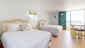 Habitación de hotel con dos camas, un balcón con mesa y vista al mar.